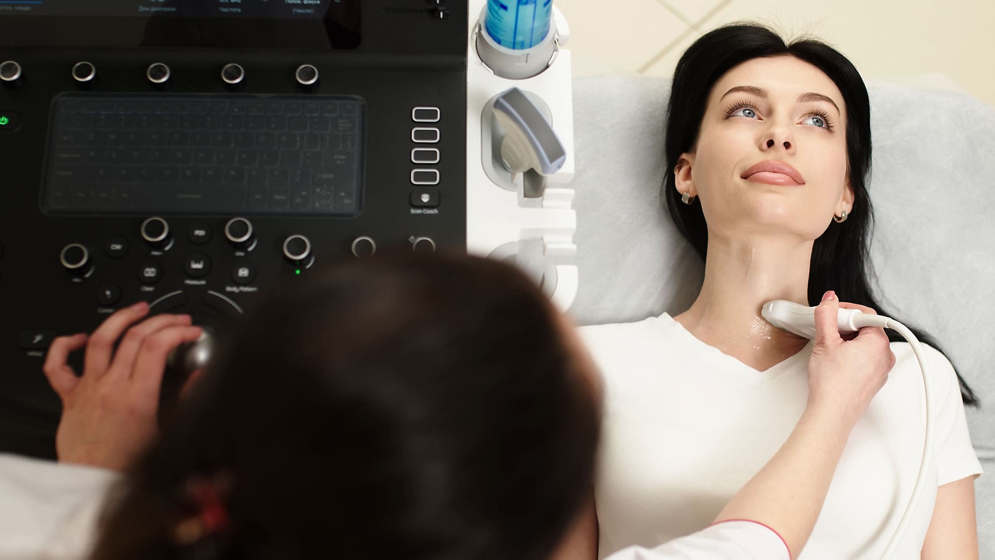 A physician performs a thyroid ultrasound on a female patient