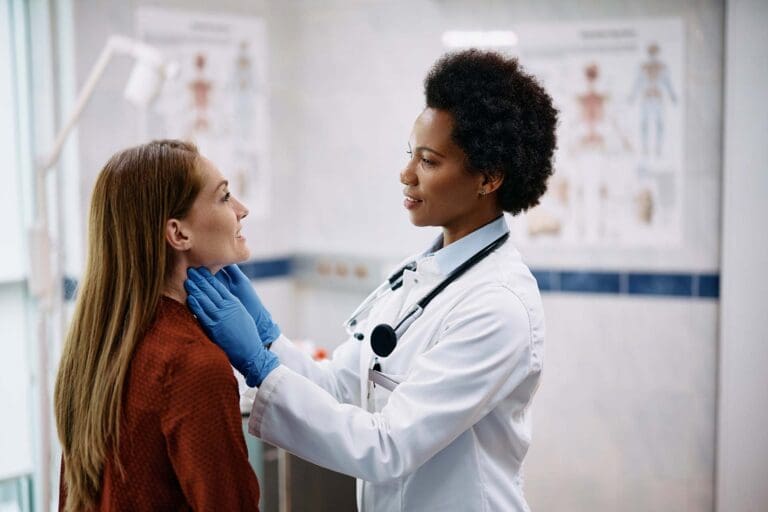 A doctor examines a patient’s thyroid in an examination room