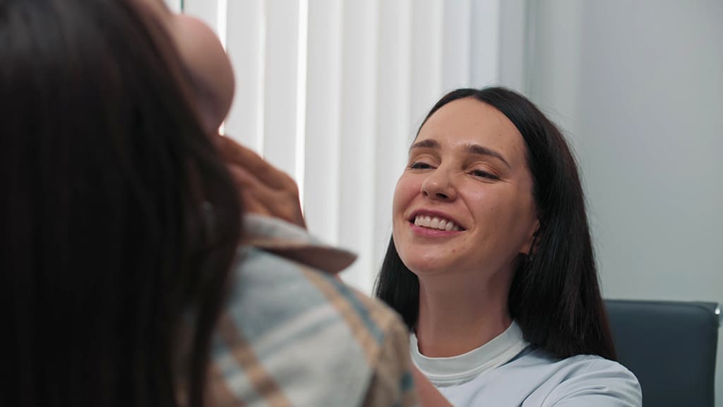 A smiling clinician performs a thyroid exam on a patient